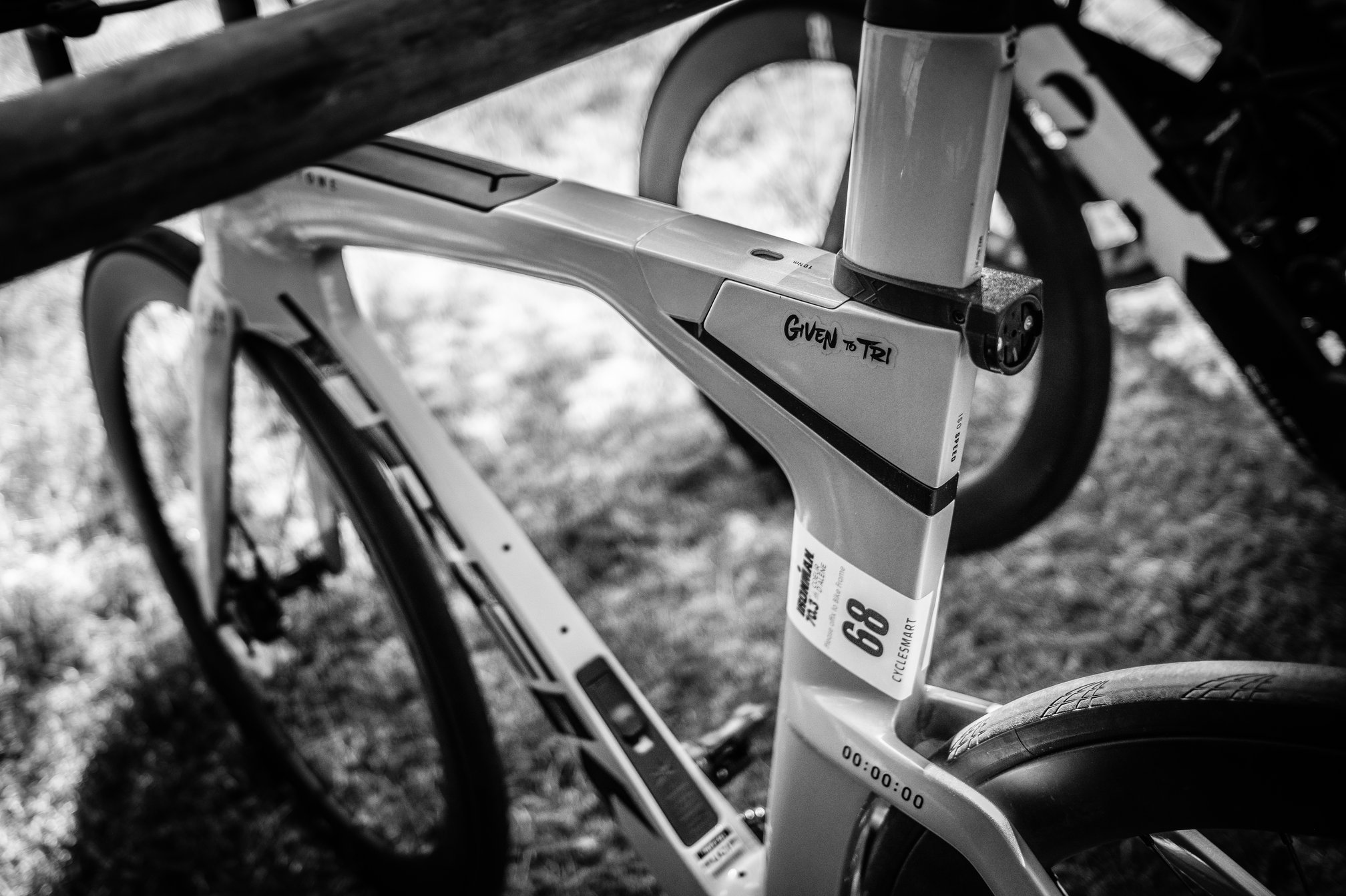 Close-up of a silver Trek Speed Concept triathlon bike with a "Given to Tri" sticker near the seat tube and a race sticker, number 68, for Ironman 70.3 Coeur d'Alene.