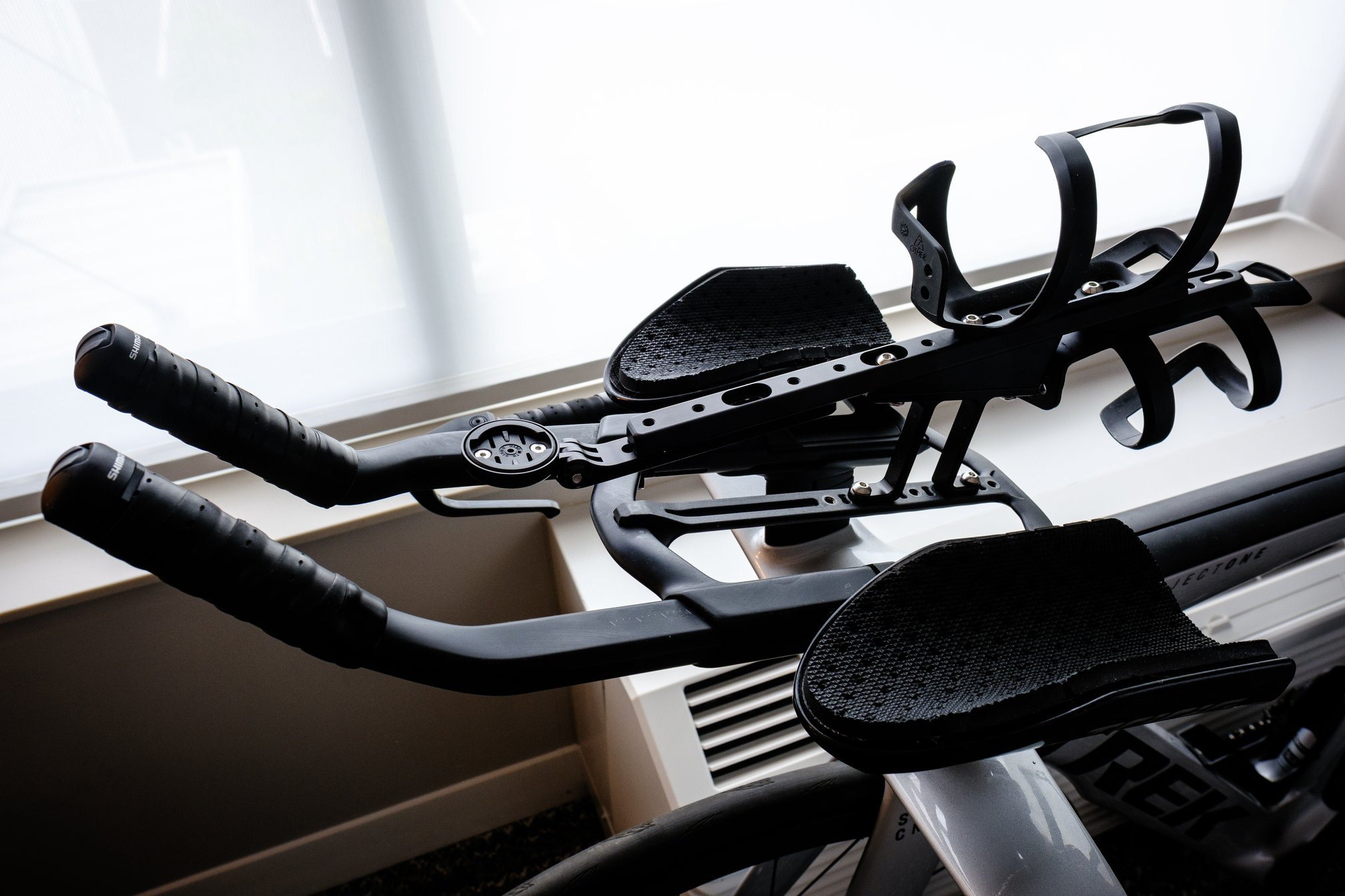 The cockpit setup of a Trek Speed Concept triathlon bike, featuring stock aero bars with TriRig arm scoops, and two Trek side-loading bottle cages mounted at the rear of a TriRig BTA riser and multi-bottle rail.